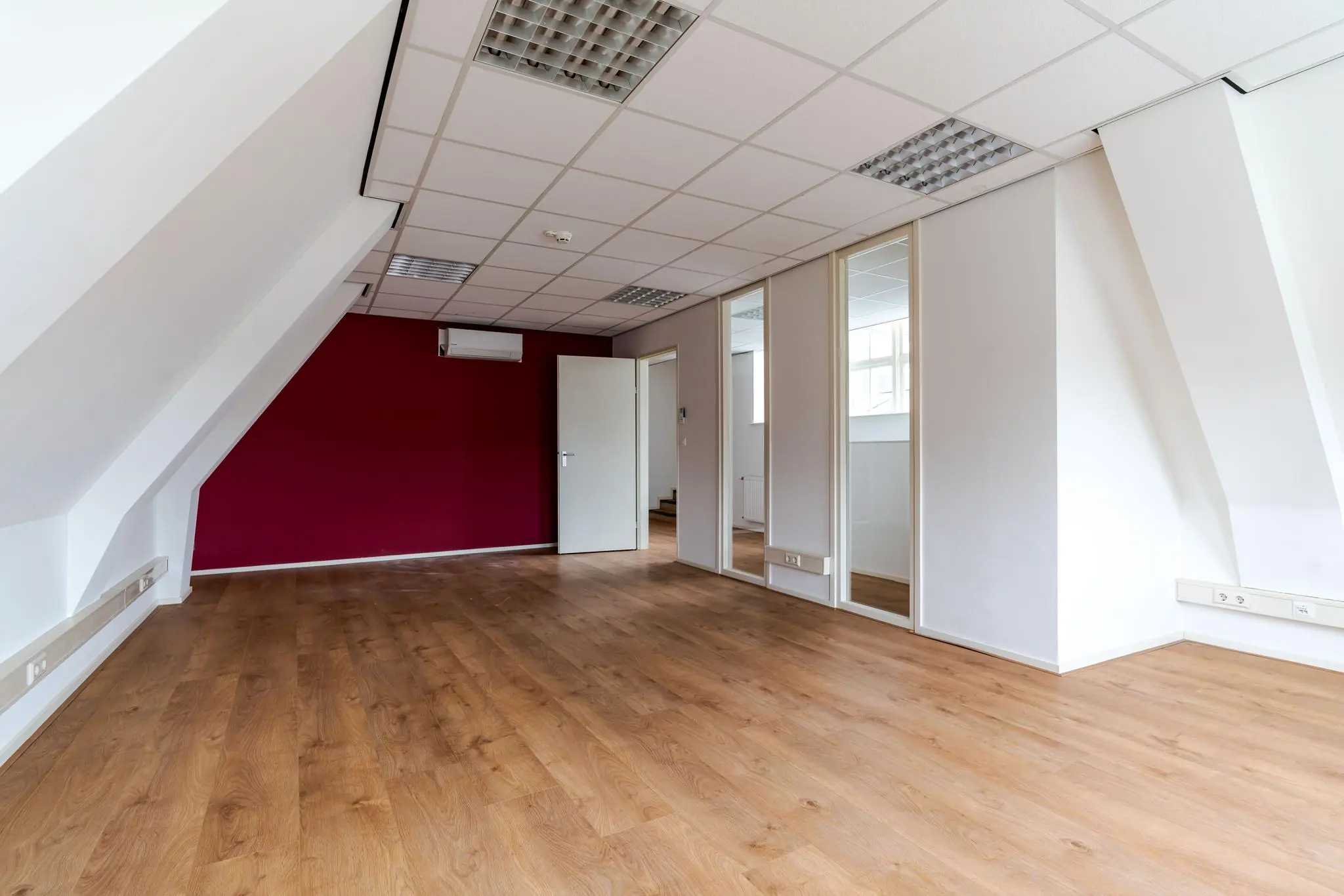 Licht kantoorruimte aan het Lange Voorhout met houten vloer, schuine wanden en een bordeauxrode accentmuur.